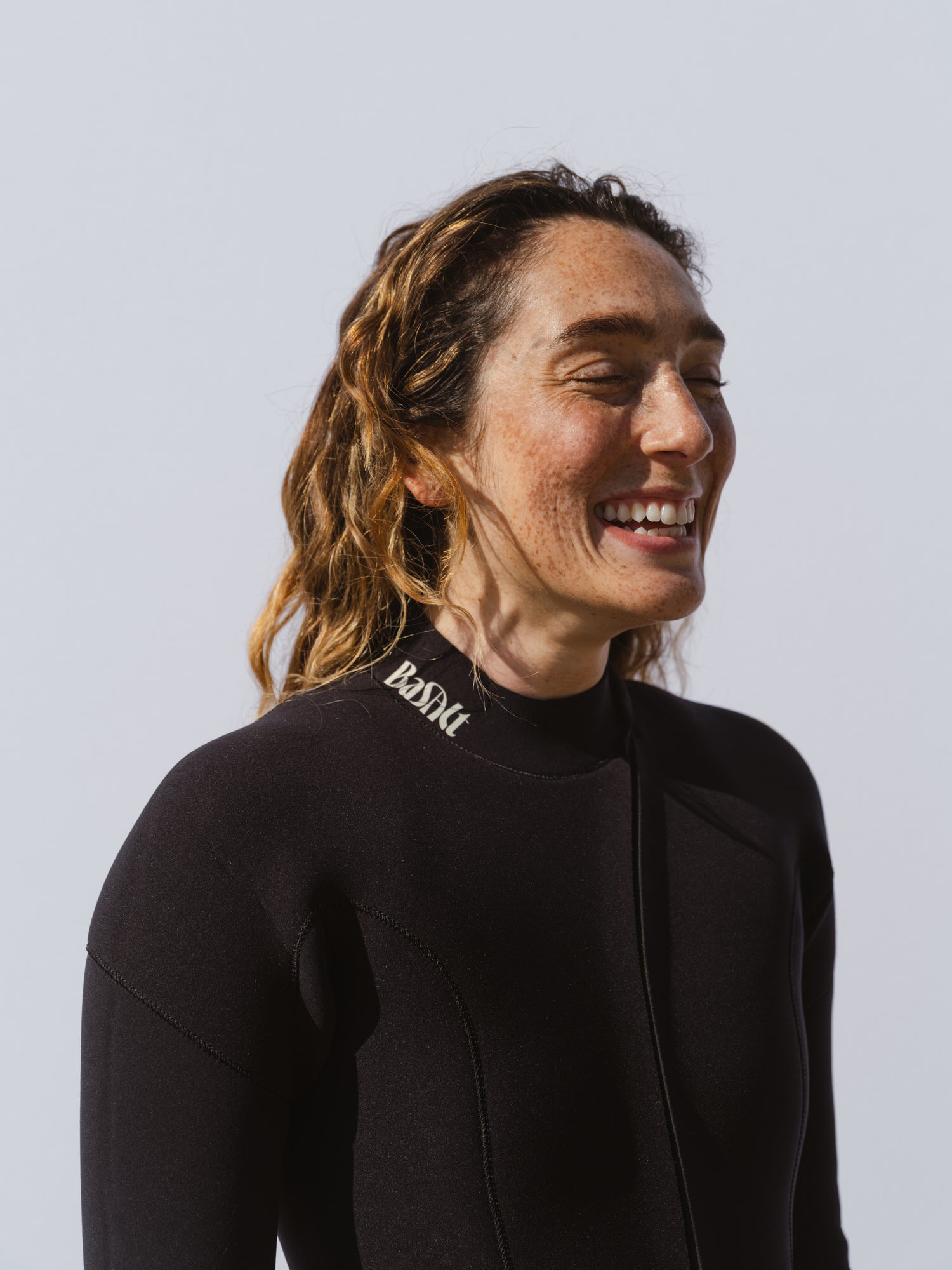 Woman smiling in a Basalt women’s jersey 4/3mm wetsuit with curved front zip and subtle Basalt logo