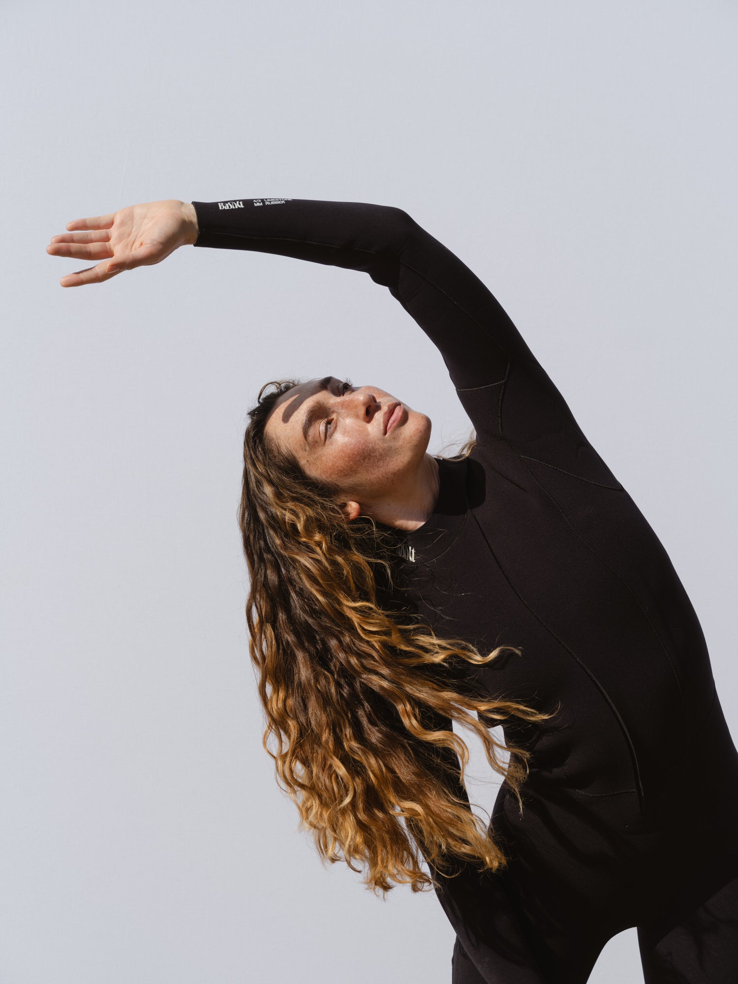 Woman stretching in a Basalt women’s 4/3mm Jersey wetsuit, showing flexibility and ease of movement.
